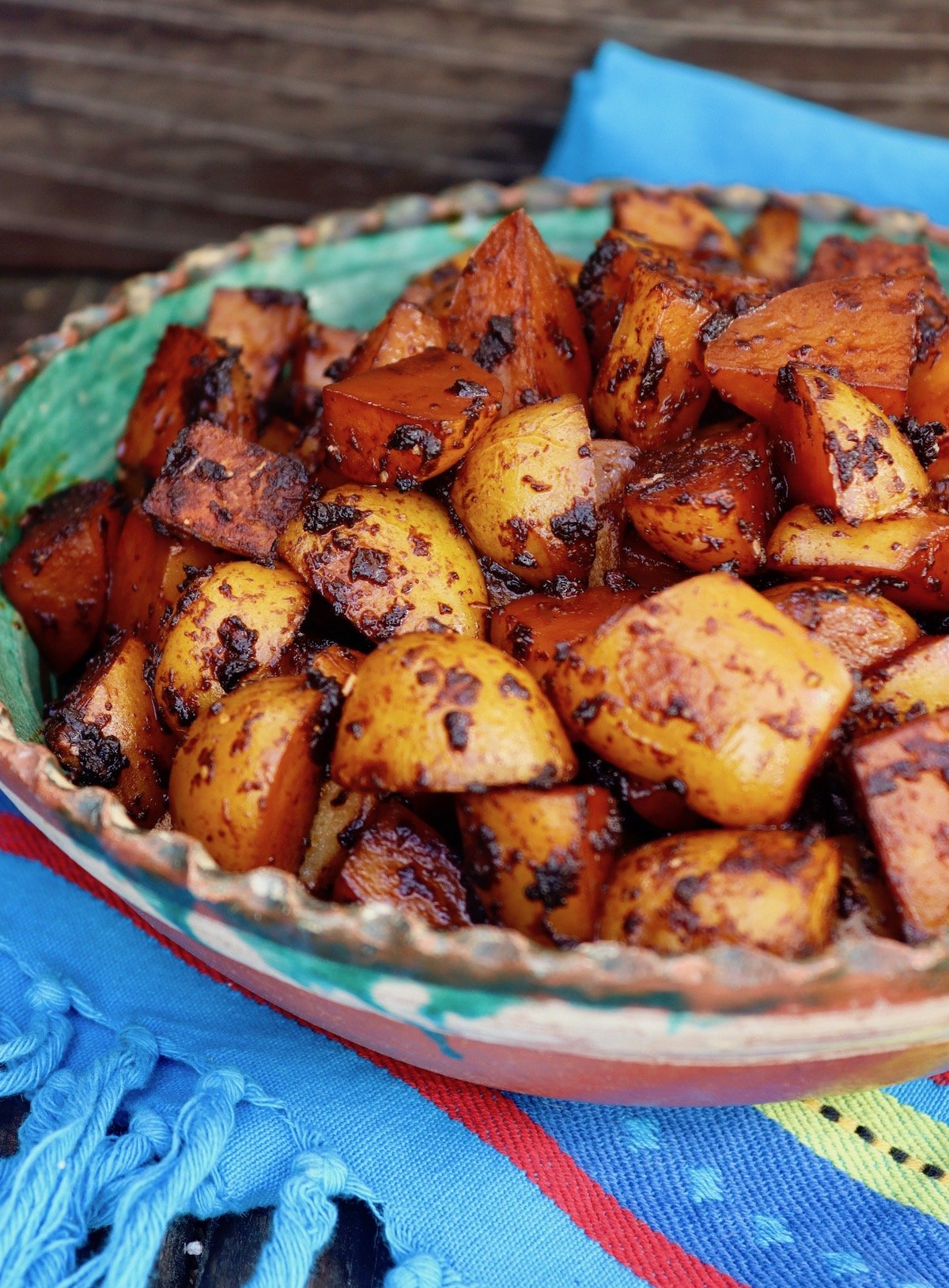 Green and terra cotta bowl filled with cubed potatoes covered in red sauce.