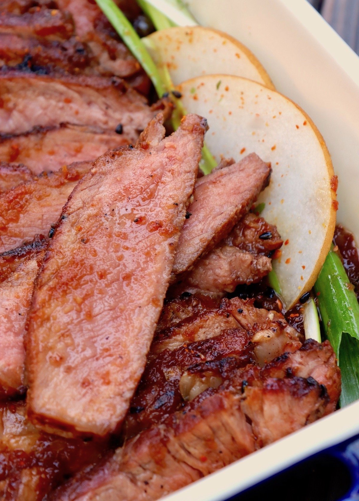 Sliced ribeye steak with a few pear slices and scallions