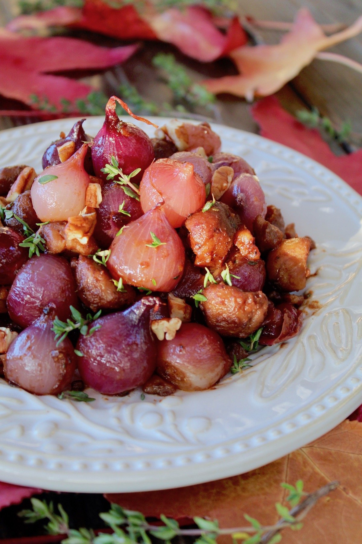 Braised Chestnuts and Pearl Onions on white plate with fresh thyme leaves