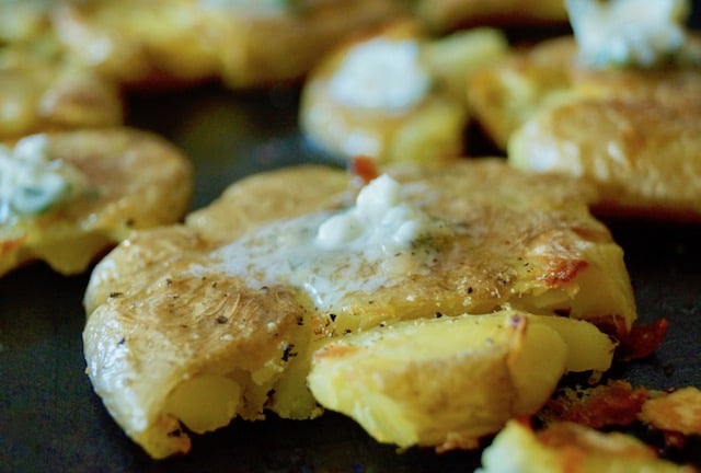 Close up of a smashed potato with herb garlic butter melting on top, on a sheet pan.