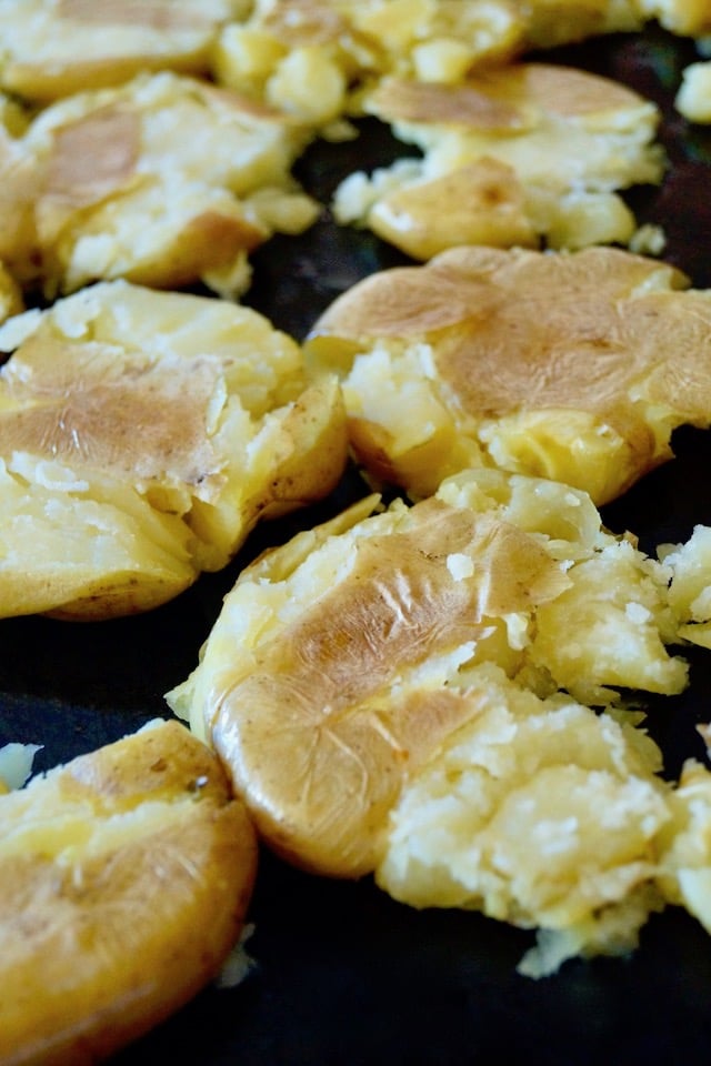 Sheet pan full with smashed potatoes.