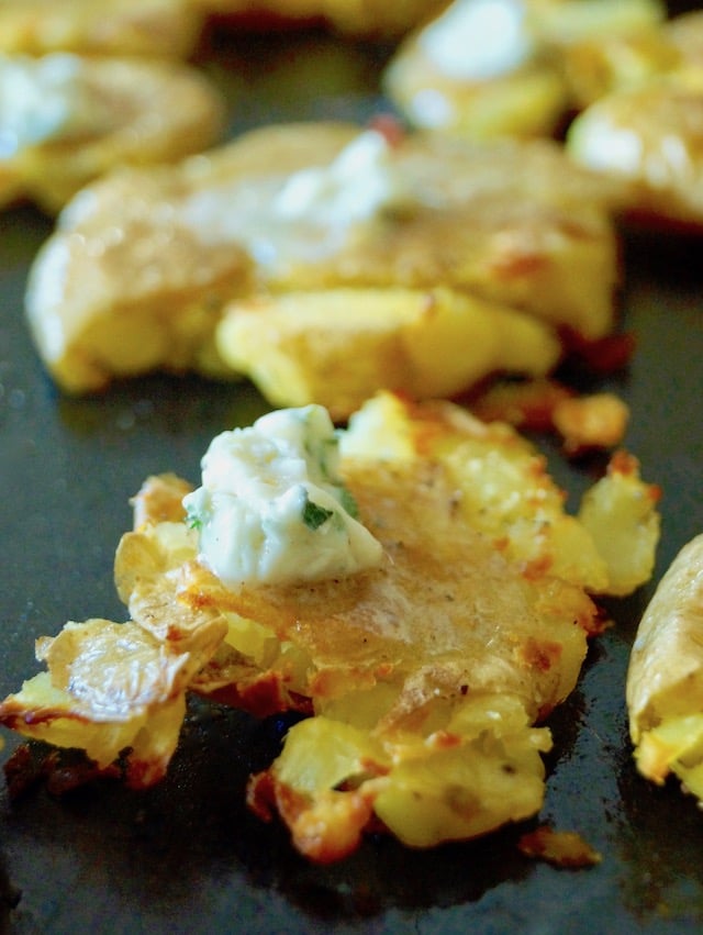 Close up of a very crispy msashed potato with butter melting on top, on a sheet pan.