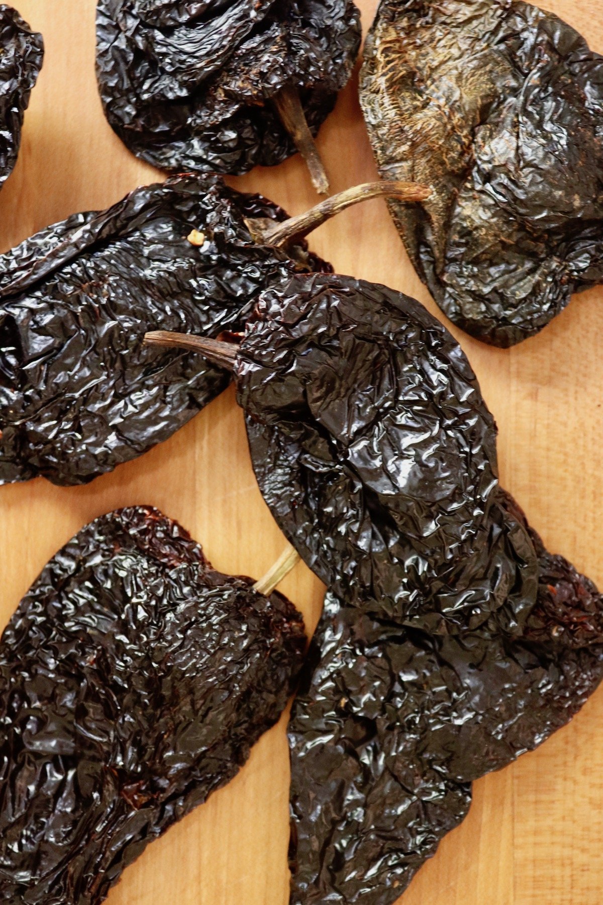 Several ancho chiles on light wood cutting board.