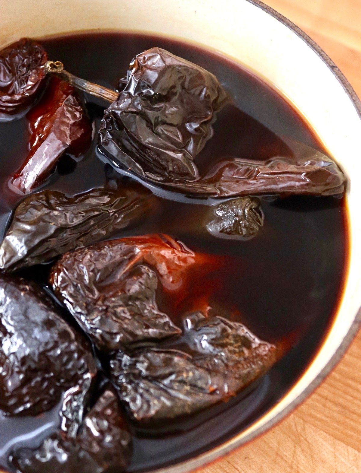 Several ancho chiles in hydrating water in pot.