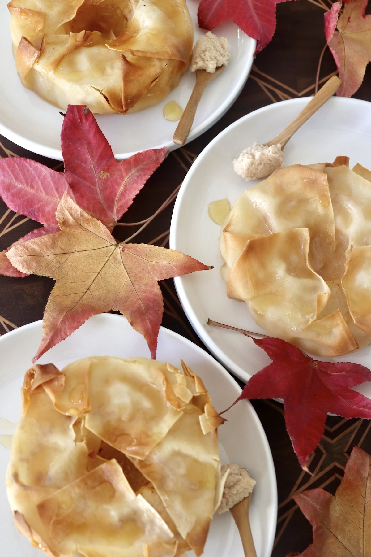 Baked-Asian-Pear-Recipe Three white plates with pastry-wrapped Asian pear halves, surrounded by maple leaves.