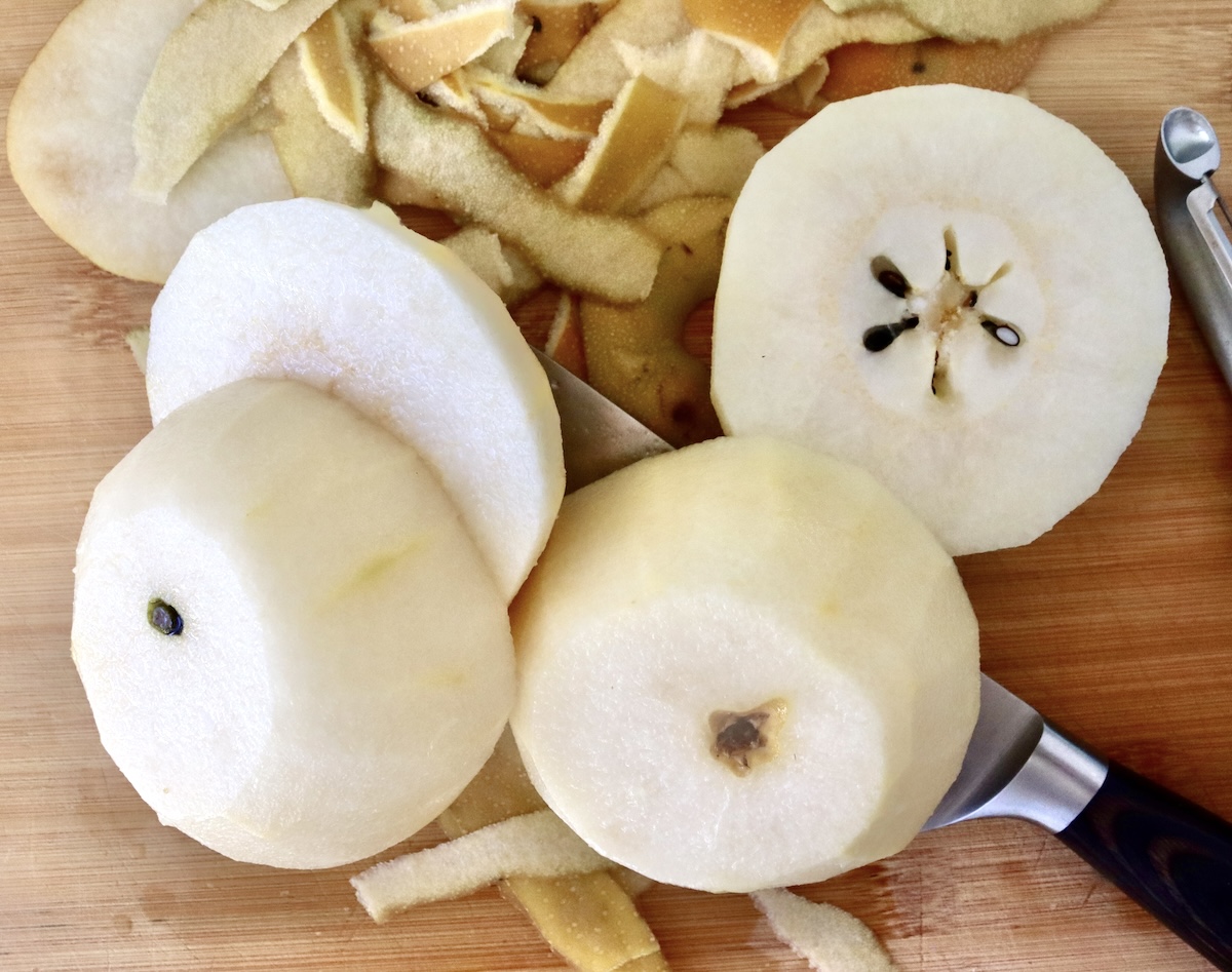 Baked-Asian-Pear-Recipe Four peeled halves of Asian pear on a cutting board with a knife and the peeels.