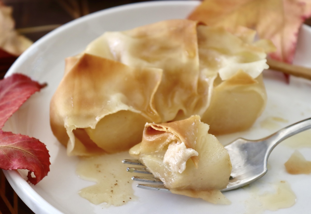 Baked-Asian-Pear-Recipe Half of a baked wonton-wrapped Asian pear on a white plate, with one bite on a fork with a bit of cream.