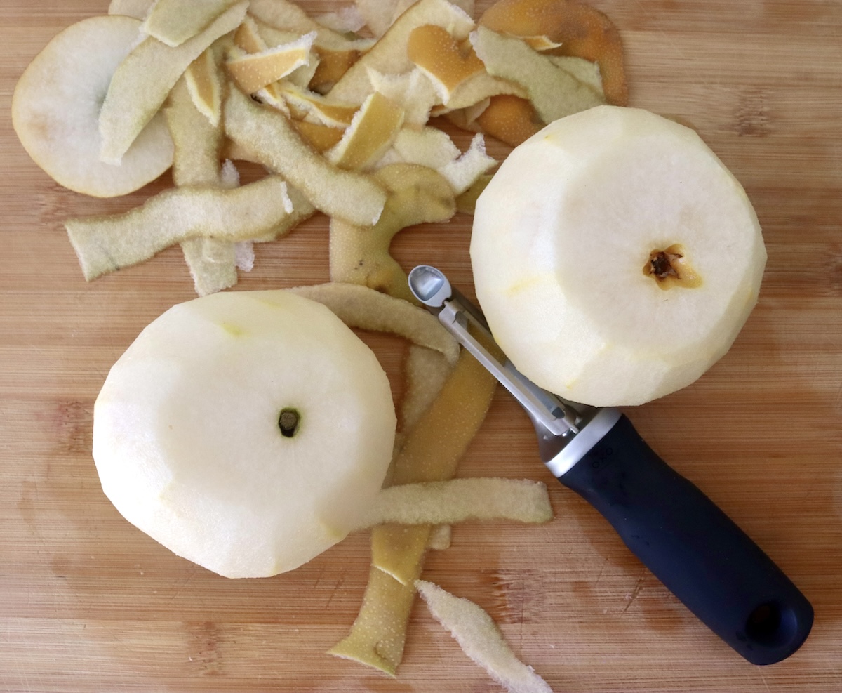 Baked-Asian-Pear-Recipe Two peeled Asian pears with a slice cut off the top of each one, on a cutting board, with the peels next to them.
