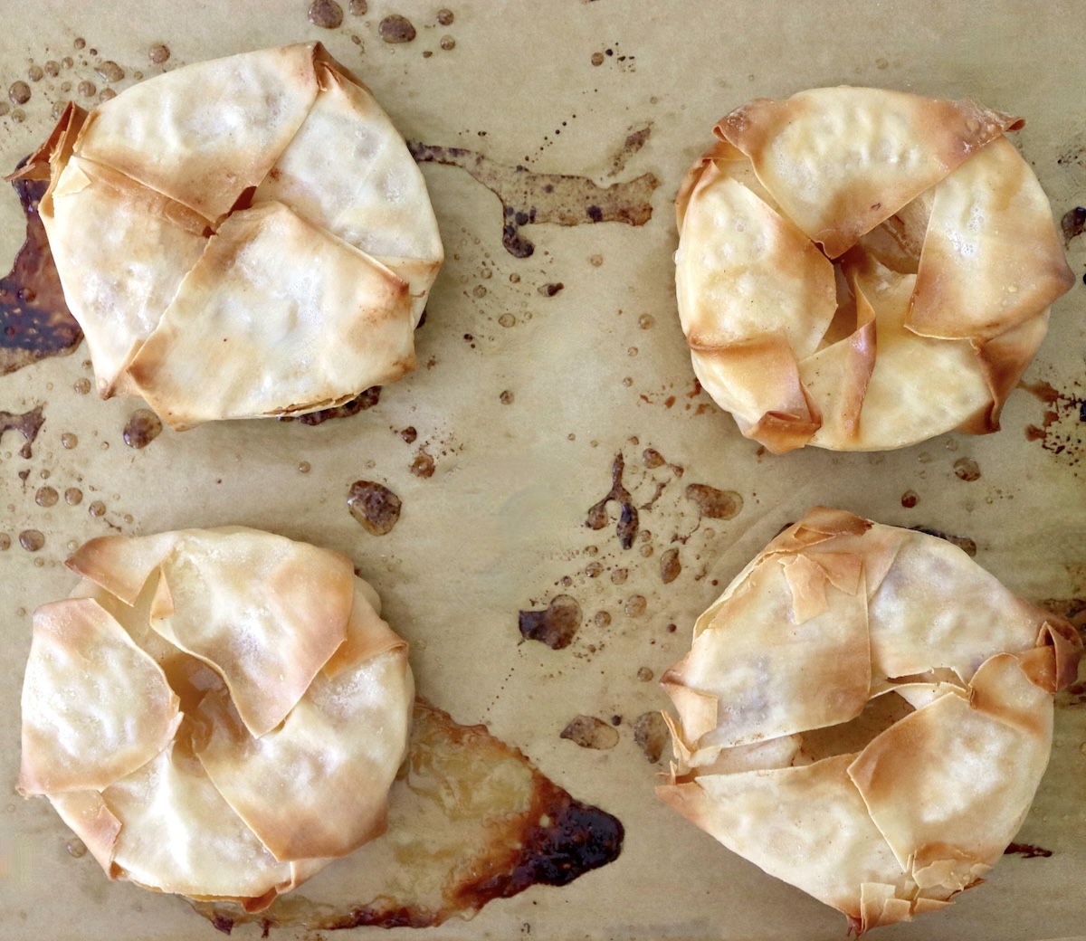Baked-Asian-Pear-Recipe Four baked golden pastry bundles of pear on a parchment-lined baking sheet.