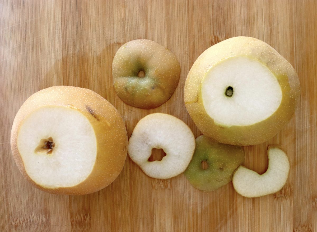 Baked-Asian-Pear-Recipe Two Asian pears with a slice cut off the top of each one, on a cutting board.