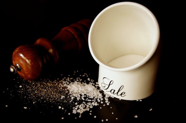 salt pig and pepper grinder with black background and salt and pepper grounds spilled out