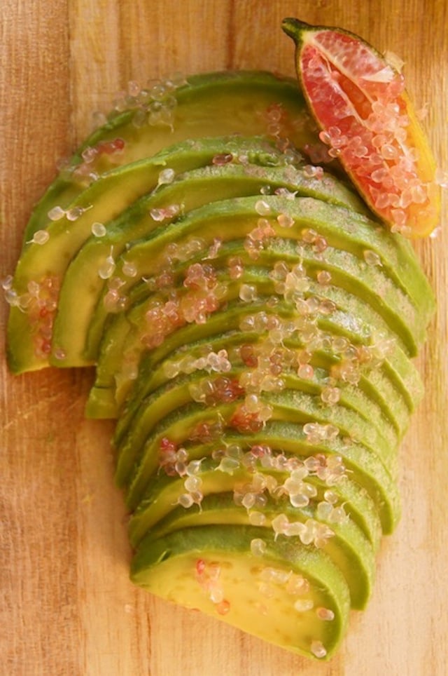 Finger Lime "beads" or "balls" of citurs strewn over a thinly sliced avocado half.