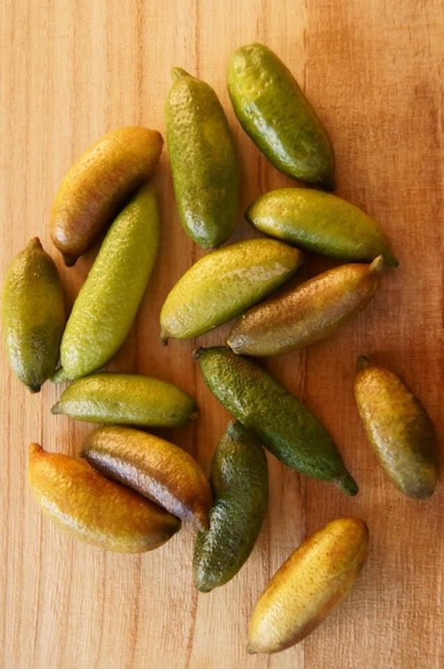 Serveral Finger Limes on a cutting board, varying in shades or green and yellow.