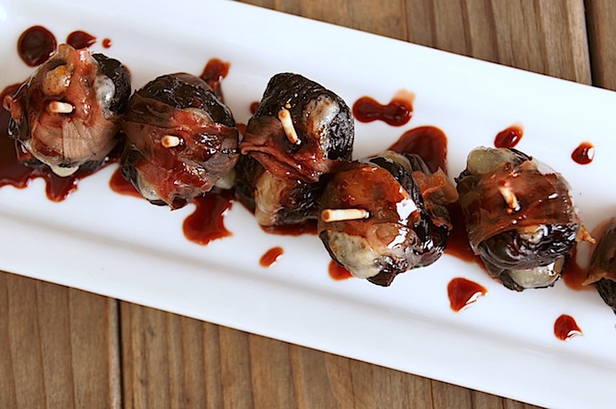 Top view of several dried fig hors d'oeuvres on a white narrow plate with toothpicks in each one,