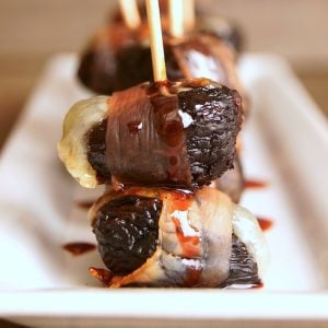 Several dried fig hors d'oeuvres on a white narrow plate with toothpicks in each one,