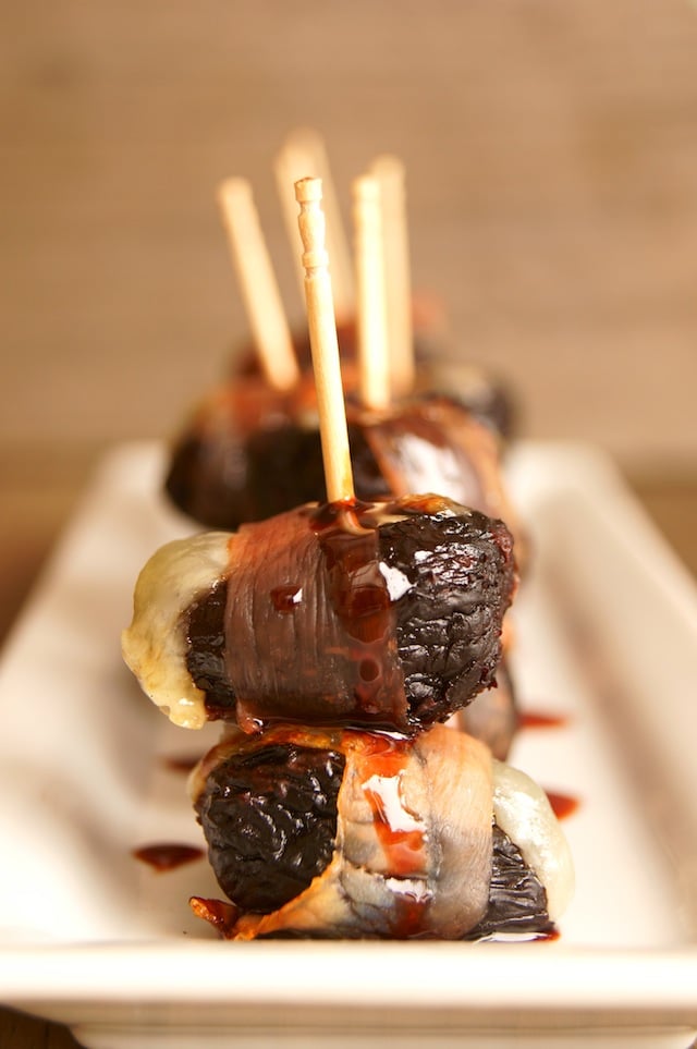 several dried figs with manchego and prosciutto with toothpicks on white plate