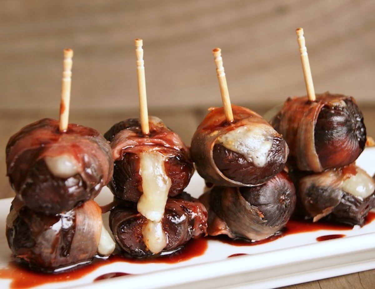 Several dried fig hors d'oeuvres on a white narrow plate with toothpicks in each one,