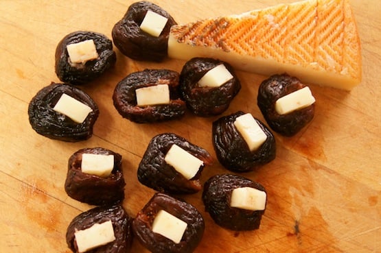 Dried figs with a wedge of cheese and small pieces of cheese on top of each fig.