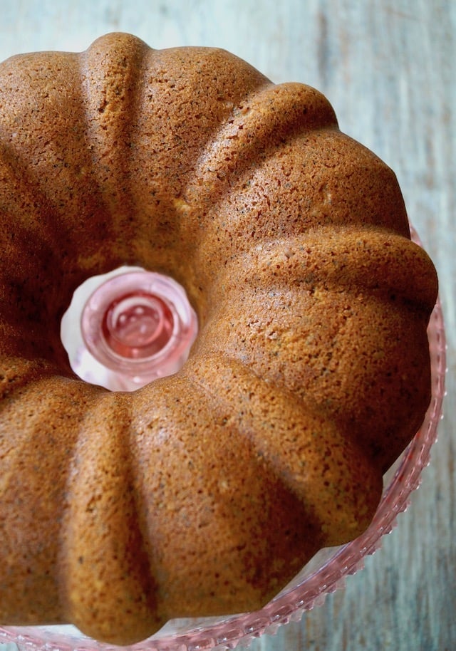 Eggnog Bundt Cake with Poppy Seeds on a pink glass cake plate without frosting.