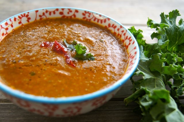 Spicy Kale Soup in a bowl with Roasted Pepper and Tomato with a fresh kale leaf next to it