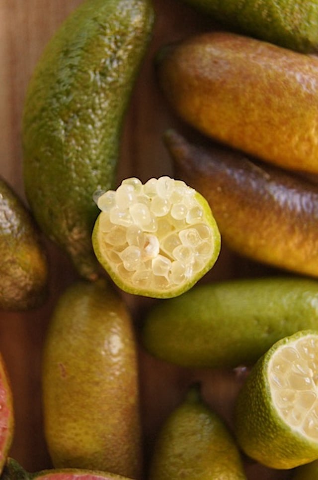 Pile of green Finger Limes, with a top view of one cut open, horizontally in the center.