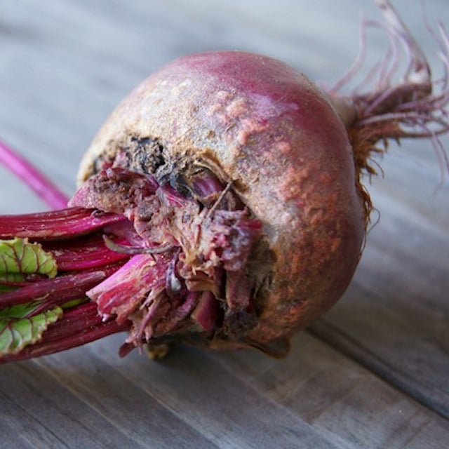 one raw beet with greens laying on it's side