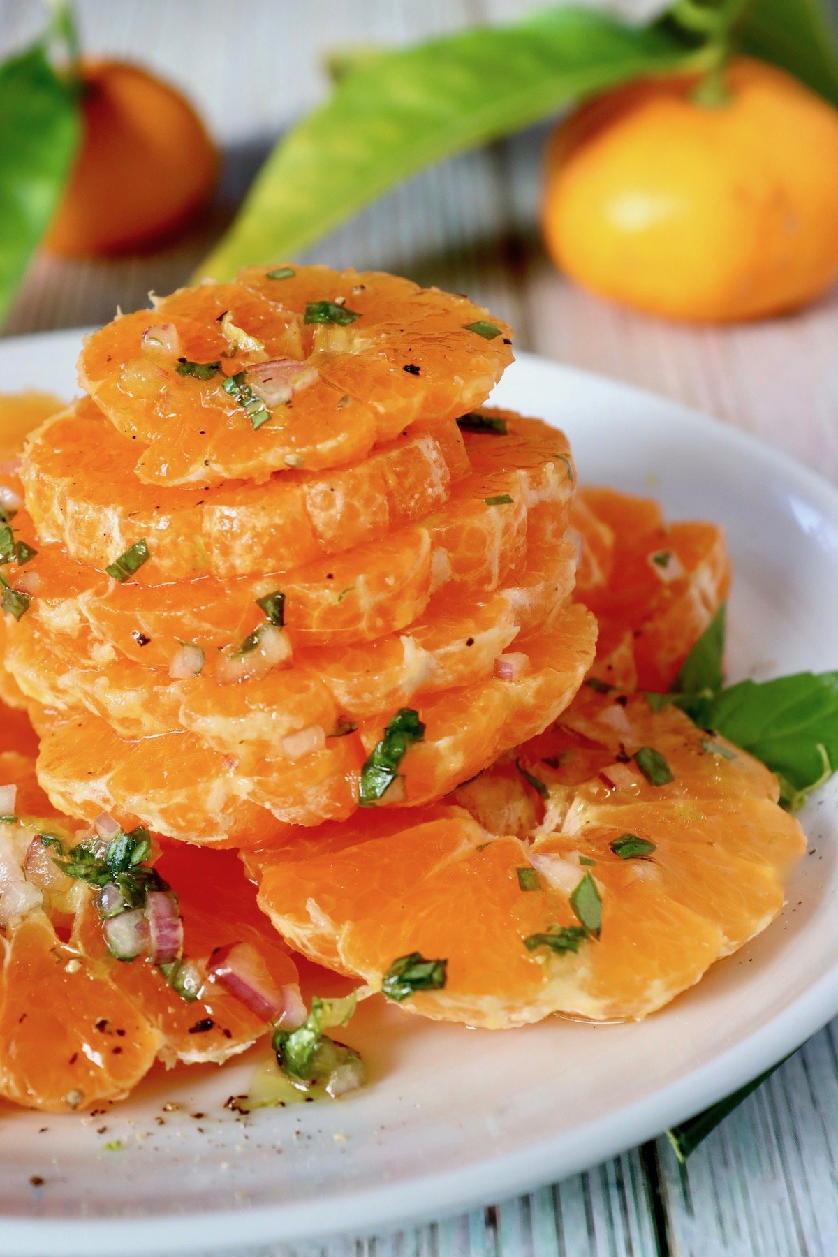 stack of sliced satsumas with bits of basil on white plate