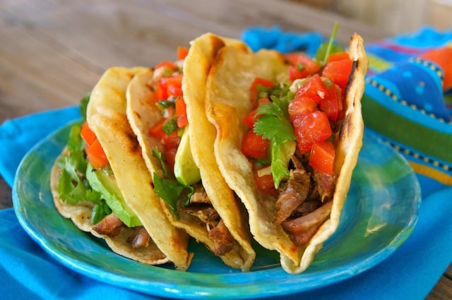 Three pork tacos with pickled tomatoes on blue plate.