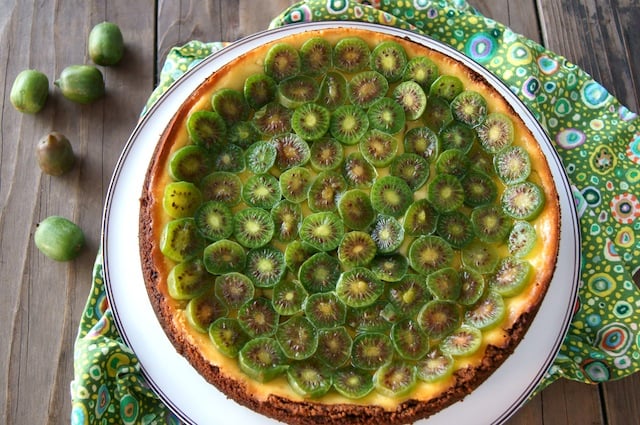 Kiwi Mascarpone Cheesecake on a white platter on a green floral cloth.