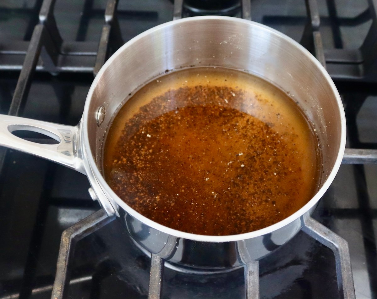 Dark vinegar mixture in a very small saucepan on a stovetop.