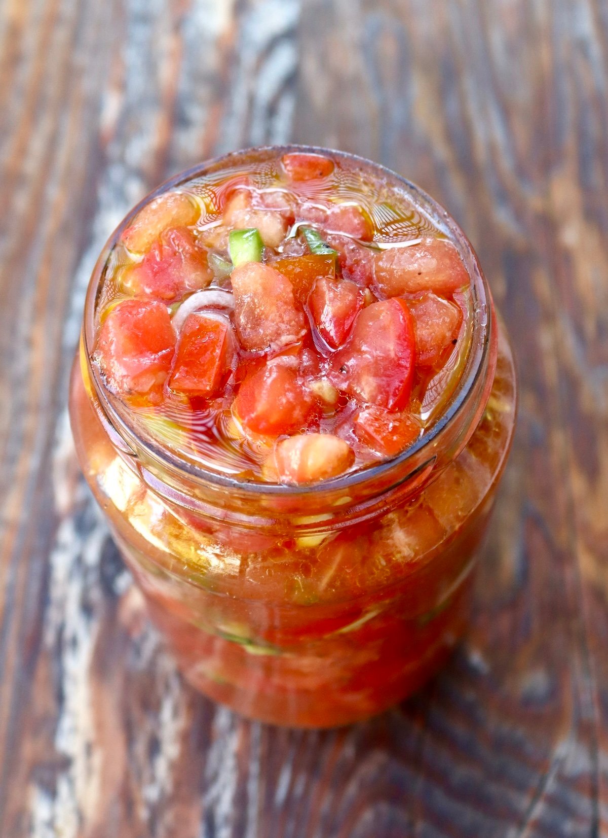 Top view of pickled tomato salsa in a jar, on wood surface.