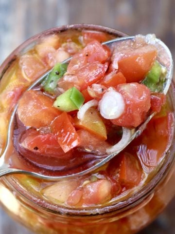 Pickled tomato salsa in a jar with a spoonful on top.