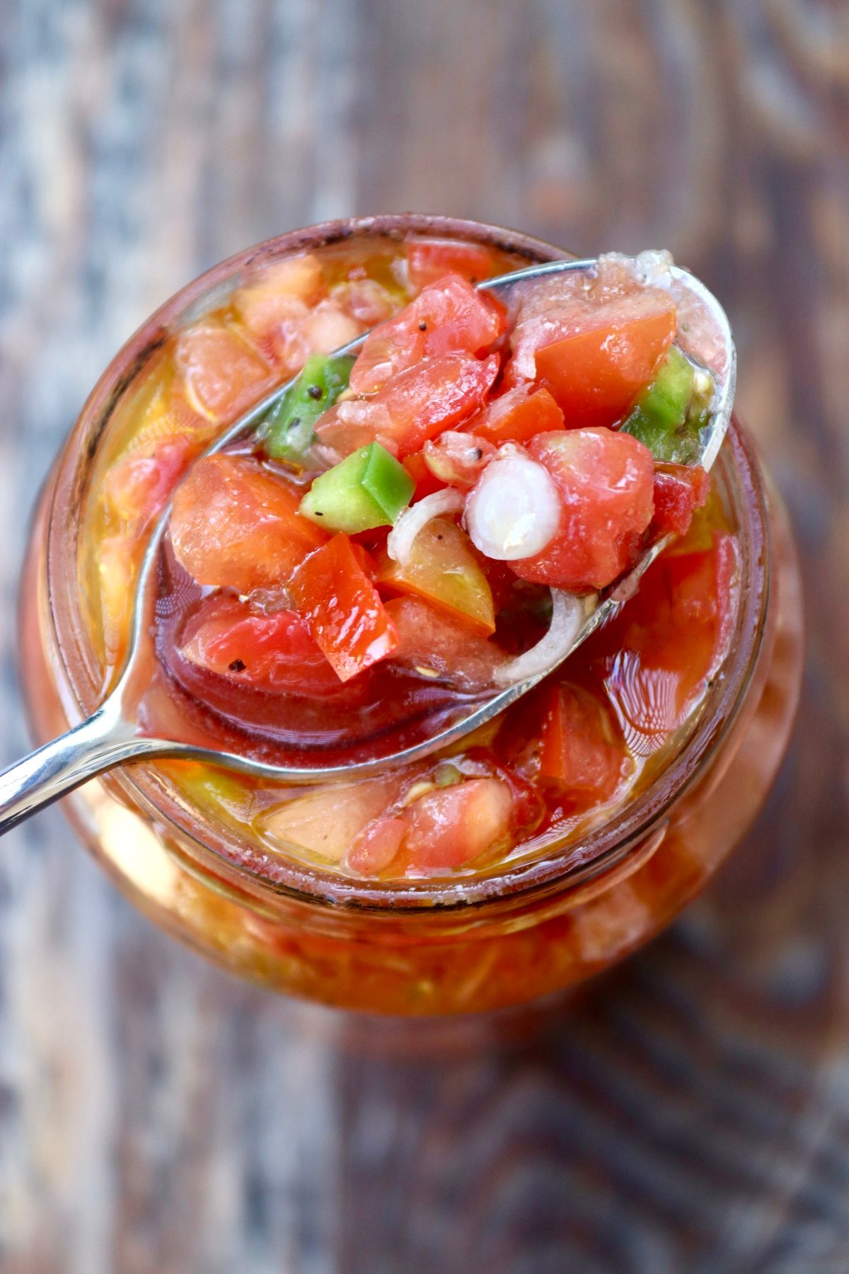 Pickled tomato salsa in a jar with a spoonful on top.