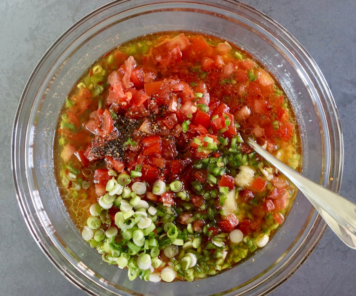Chopped tomato, onion, green pepper and garlic in a large glass bowl with vinegar mixture poured over it.