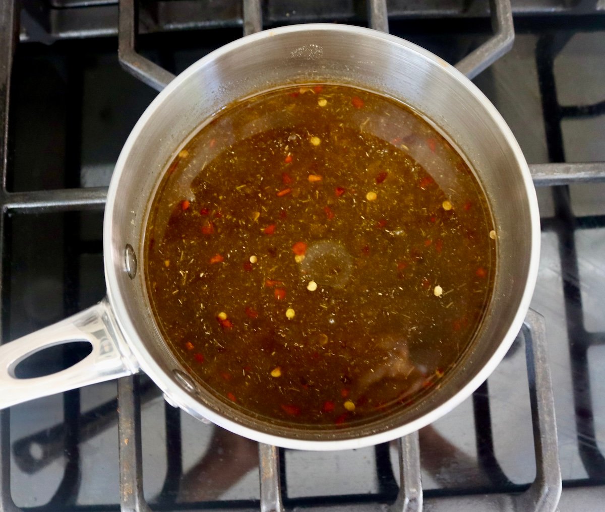 Dark and slightly cloudy vinegar mixture in a very small saucepan on a stovetop.