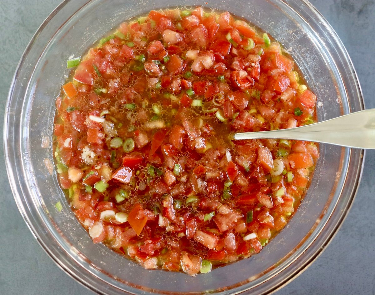 Chopped tomato, onion, green pepper and garlic in a large glass bowl mixed with pickling liquid and olive oil.