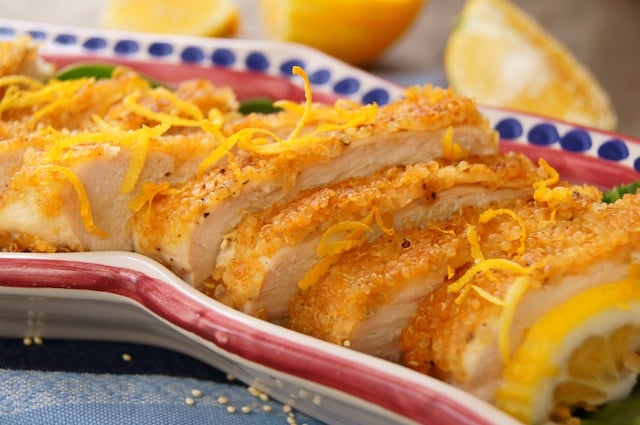 Several slices of quinoa fried chicken with lots of lemon zest on a red-rimmed, narrow plate.