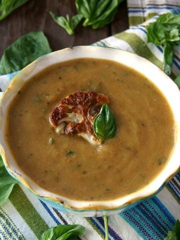 Roasted Cauliflower Basil Soup in a bowl with a cream-colored rim and a piece or roasted cauliflower and a basil leaf on top