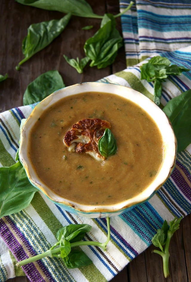 Roasted Cauliflower Basil Soup in a bowl with a cream-colored rim and a piece or roasted cauliflower and a basil leaf on top