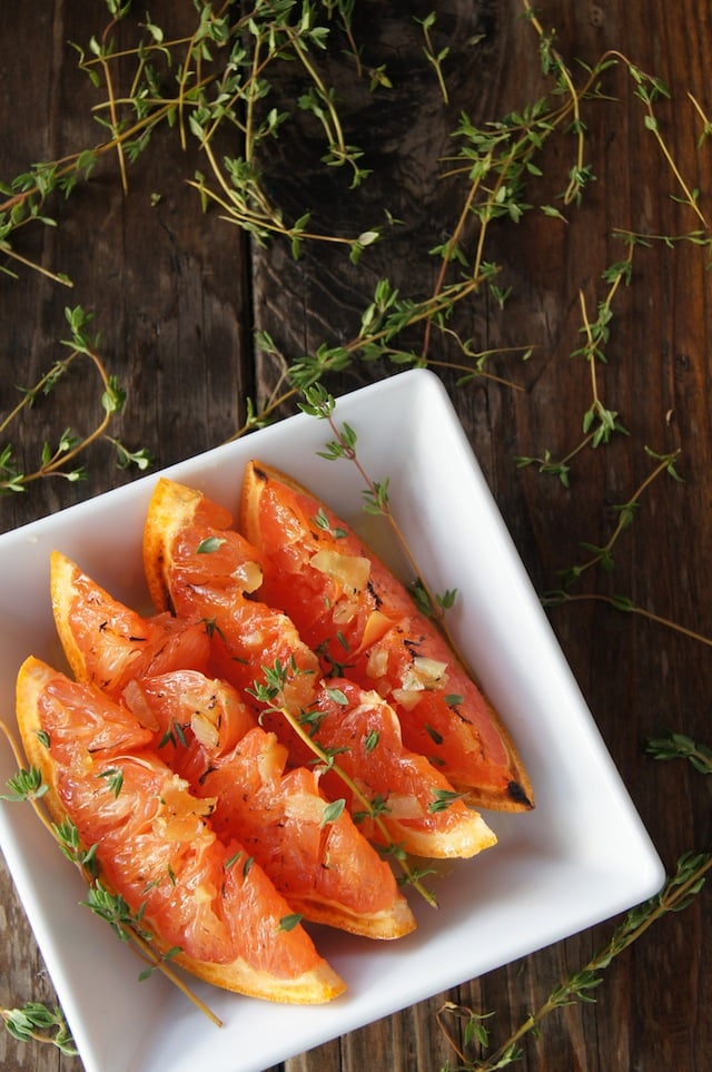 Broiled Grapefruit Slices with honey a square white dish with fresh thyme.