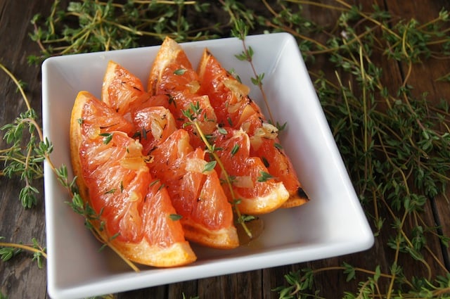 Broiled Grapefruit Slices with honey in a square white dish with dozens of fresh thyme sprigs around it