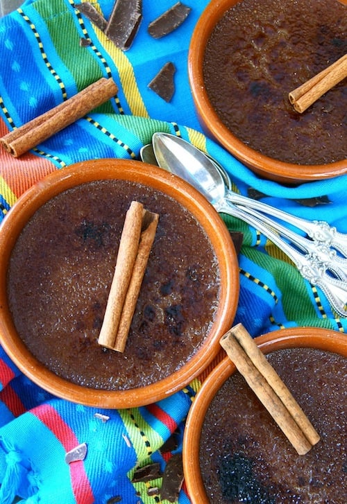 Three Mexican Chocolate Creme Brulee in terra cotta ramekins with cinnamon sticks.