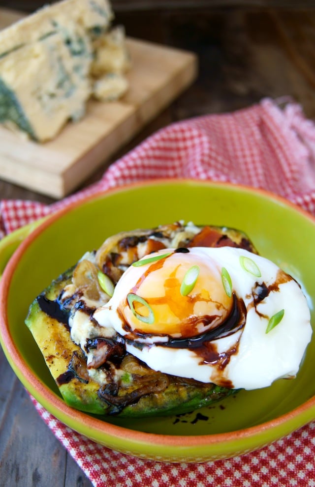 Grilled Avocado with Egg and Bacon Compote in a green bowl with Kerrygold Cashel Blue cheese behind it