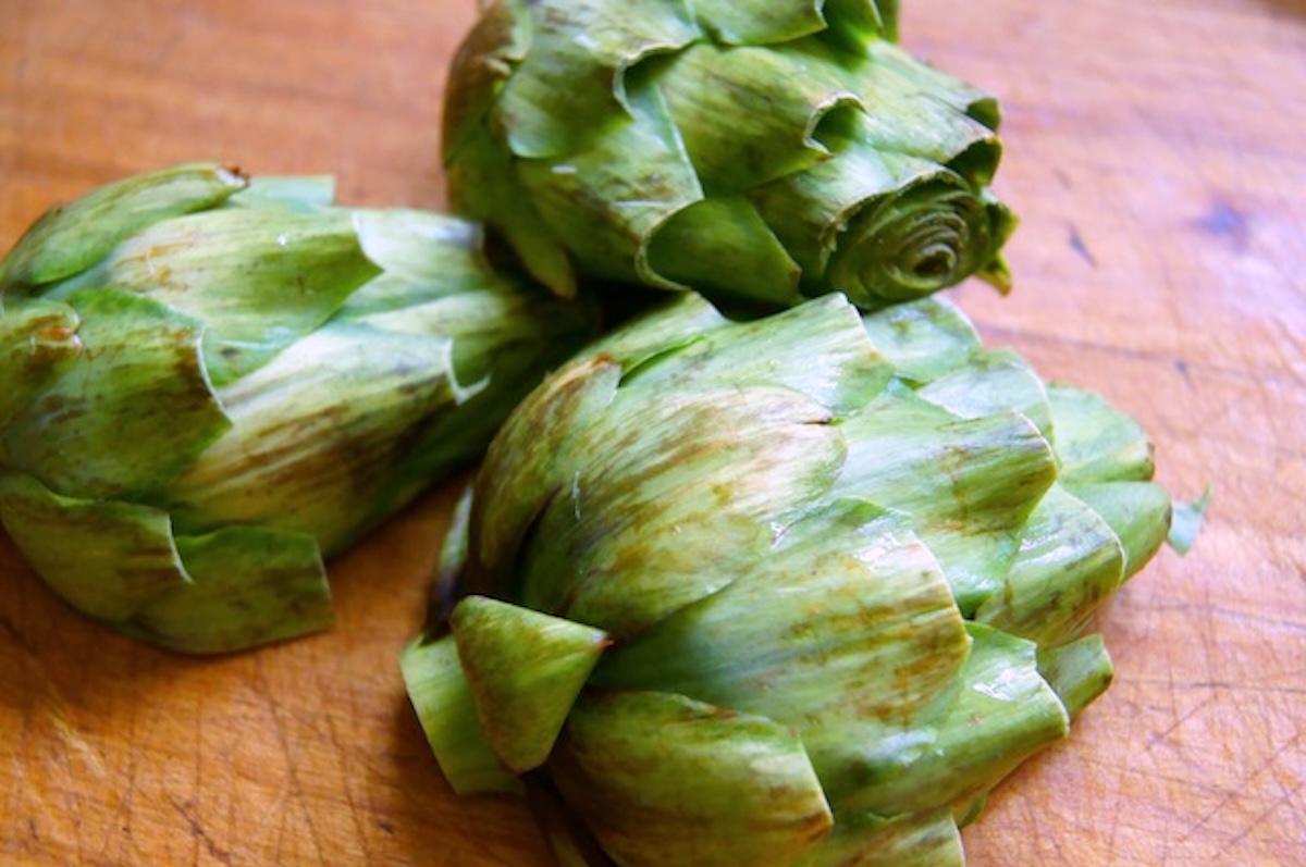 How-to-Grill-Artichokes (Smoky and Tender) Several artichoke halves with the round side up, on a wood surface.