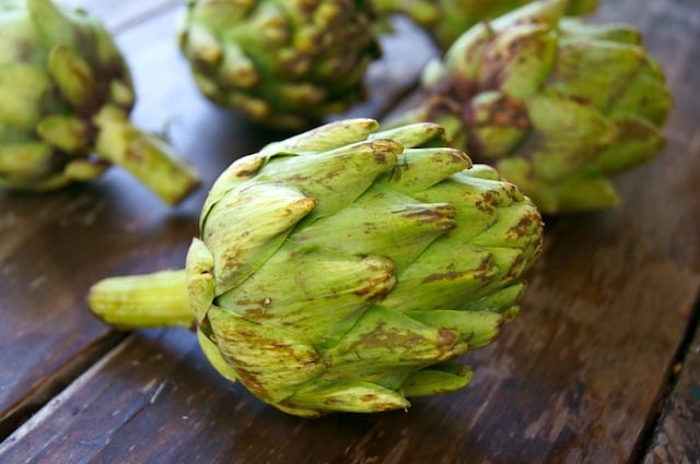 one whole raw artichoke on wooden surface