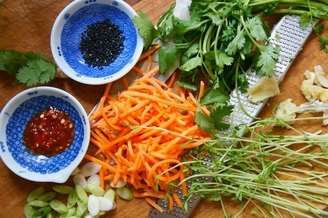 carrots, chili paste, black sesame seeds and greens on cutting board for Shirataki noodle stir-fry