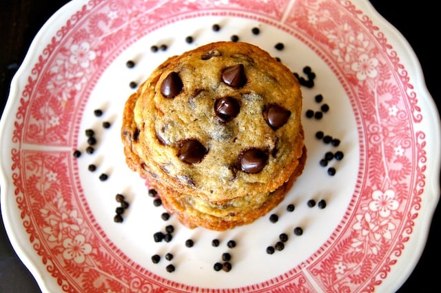 Kampot Black Pepper Chocolate Chip Cookies on a red-rimmed plate with peppercorns surrounding it. 