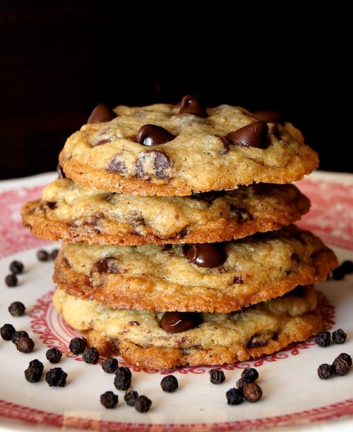 Stack of 4 Kampot Black Pepper Chocolate Chip Cookies on a white and red plate with peppercorns.