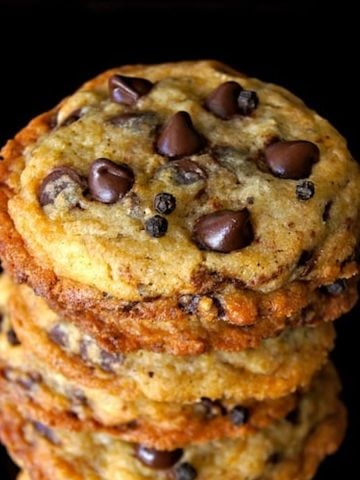 Tall stack of chocolate chip cookies with black peppercorns.