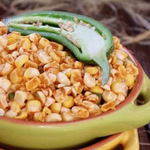 Green bowl filled with fire roasted corn and half of a raw jalapeno on wood.